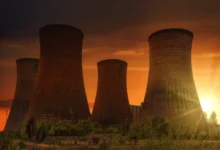 A row of tall industrial cooling towers silhouetted against a fiery sunset, showcasing a key component of Russia's energy sector.