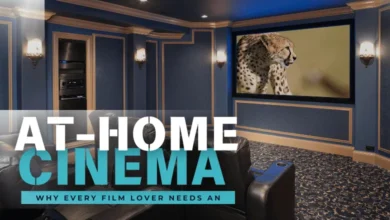 A sophisticated home cinema with plush seating faces a large screen displaying a cheetah. Elegant sconces flank the screen in a richly colored room with paneled walls.