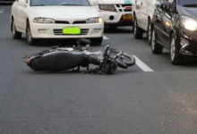 Damaged motorcycle on road after an accident, cars in background. Emphasizing road safety and accident prevention.