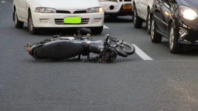 Damaged motorcycle on road after an accident, cars in background. Emphasizing road safety and accident prevention.