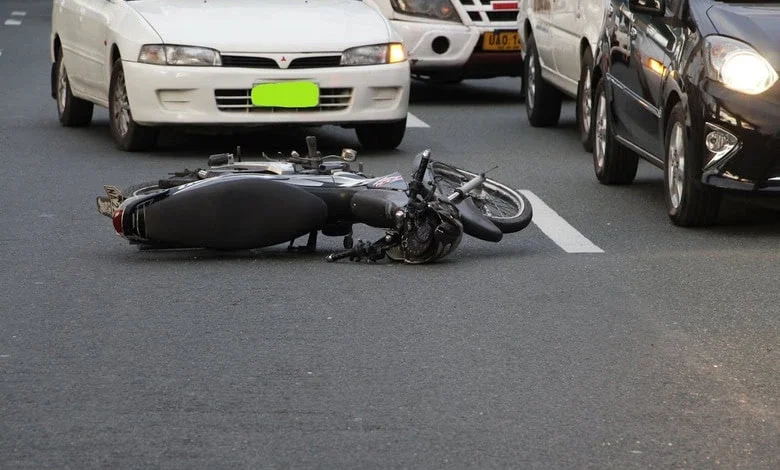 Damaged motorcycle on road after an accident, cars in background. Emphasizing road safety and accident prevention.