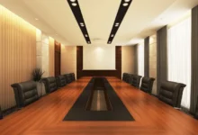 Spacious boardroom with long wooden table, black leather chairs, modern lighting, and a blank projector screen for presentations.