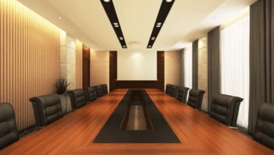 Spacious boardroom with long wooden table, black leather chairs, modern lighting, and a blank projector screen for presentations.