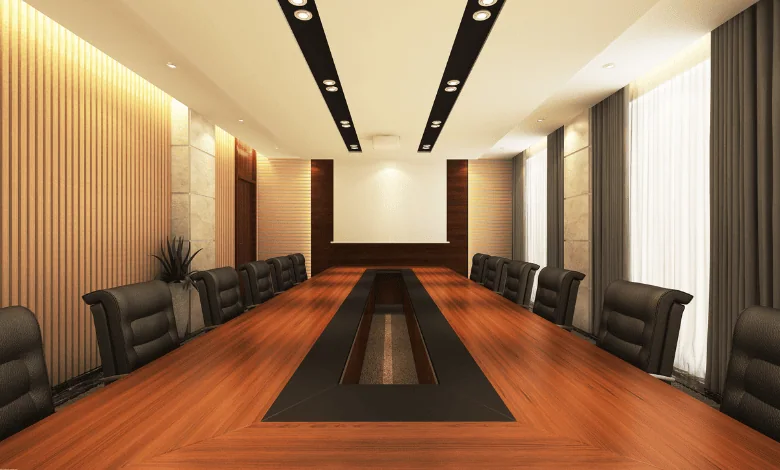 Spacious boardroom with long wooden table, black leather chairs, modern lighting, and a blank projector screen for presentations.