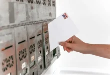 Hand inserting a letter with an American flag stamp into a row of mailboxes.