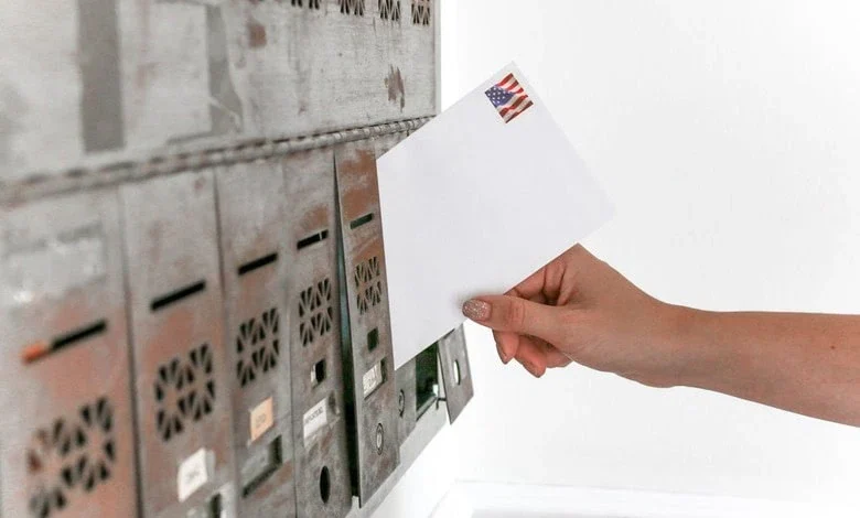 Hand inserting a letter with an American flag stamp into a row of mailboxes.