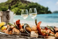 Seafood platter with lobster, shrimp, mussels, and fish served on a beach with wine and ocean view.