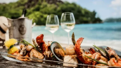 Seafood platter with lobster, shrimp, mussels, and fish served on a beach with wine and ocean view.