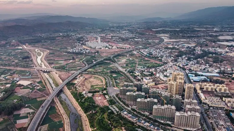 Aerial view of an urban area with high-rise buildings, highways, and suburban surroundings with greenery and small homes.